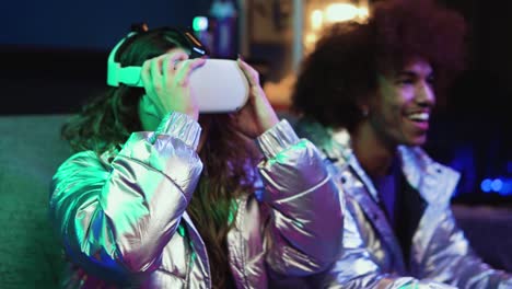 Cheerful-woman-putting-on-VR-goggles-in-dark-room-with-neon-lights