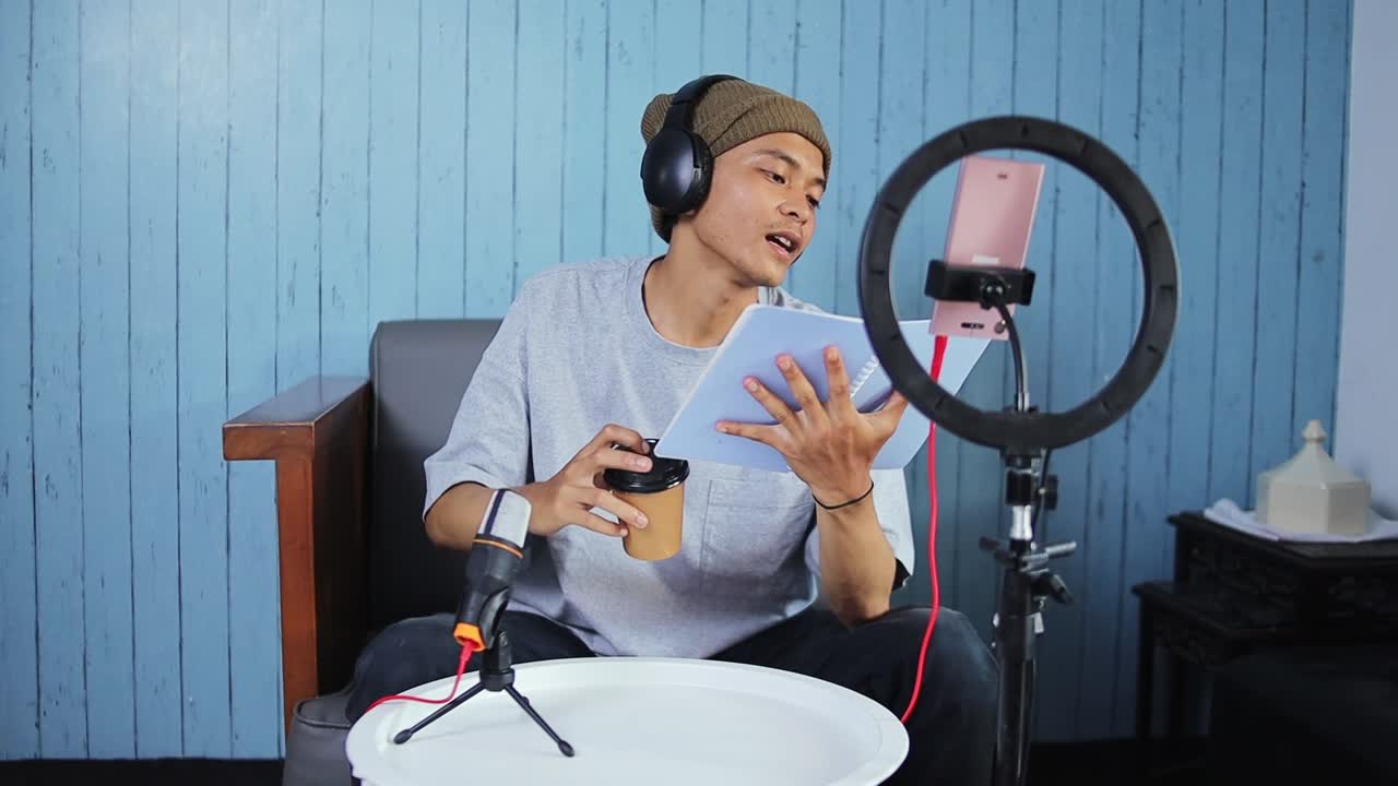 Young content creator with headphones and coffee prepares to record holding tablet and microphone