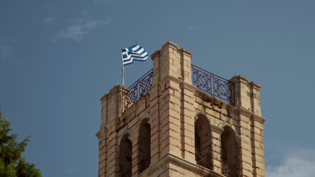 Griechische Flagge weht in Zeitlupe auf einem alten Turm vor blauem Himmel
