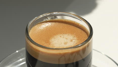 Freshly-made-hot-espresso-coffee-in-transparent-glass-on-saucer-under-sunlight---push-focus