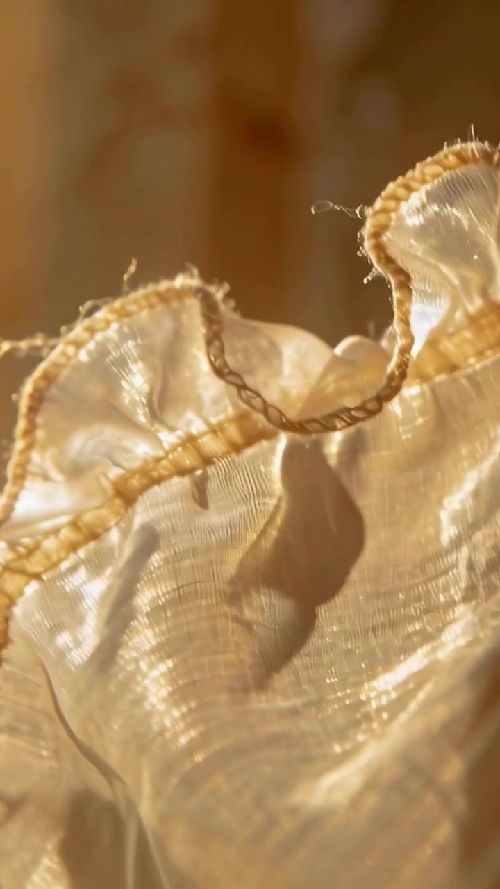 Video verticale: Bordo arricciato dorato increspato dalla luce del sole, bordo intrecciato che si solleva, fibre illuminate alla finestra.