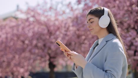 woman with headphones and phone in a spring park
