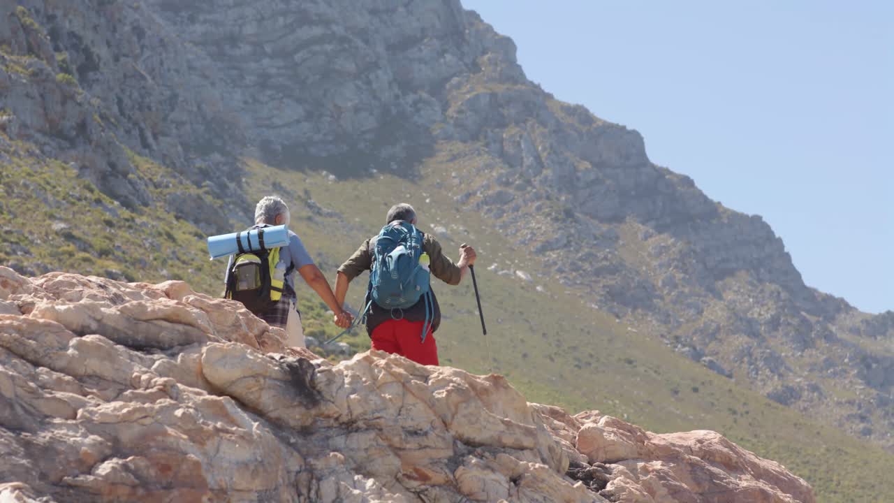 una pareja biracial en las montañas haciendo senderismo con palos de trekking, en cámara lenta.
