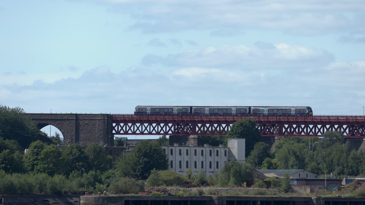 Passenger train travels across iconic red iron bridge, wide scenic view, daylight, steady camera