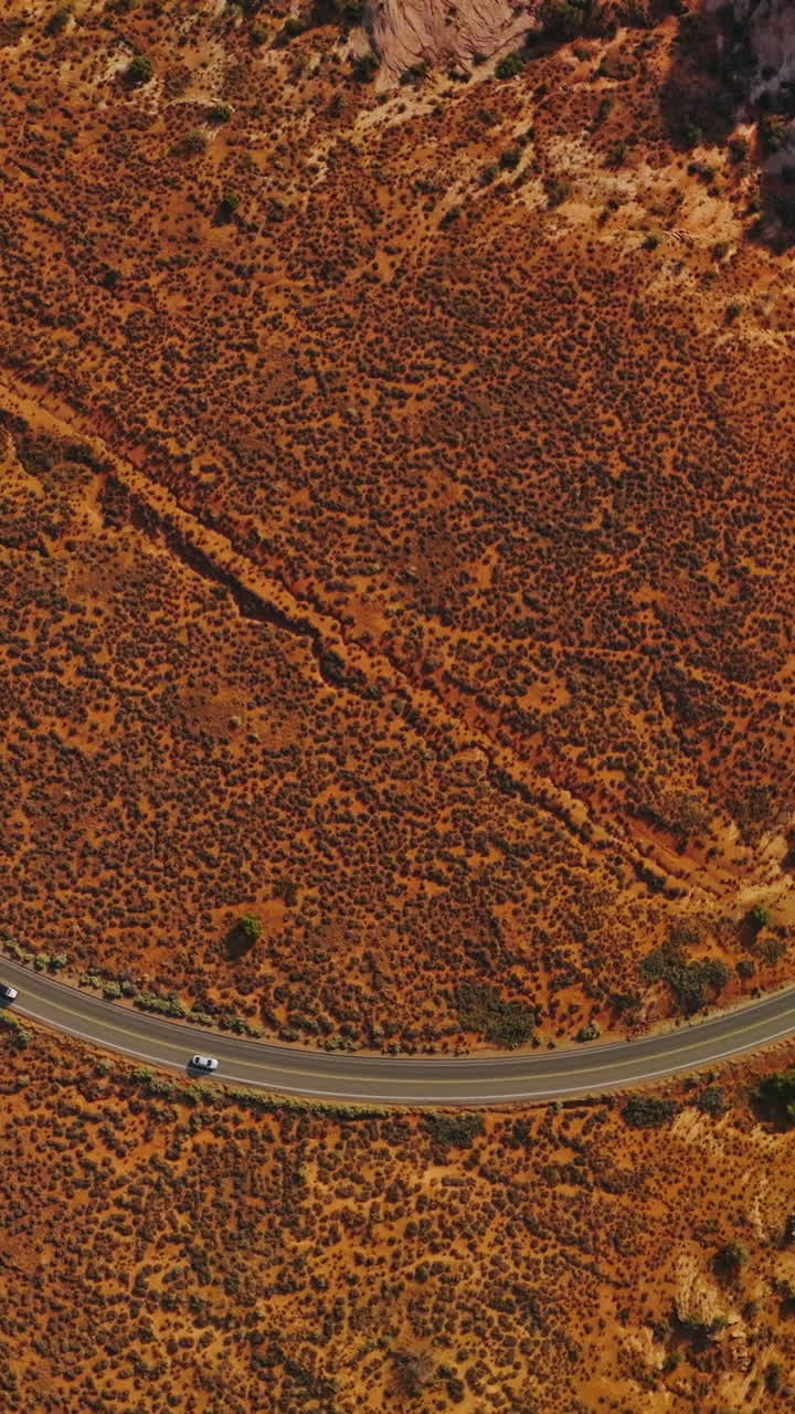 Curvy road through a desert near the weird rocks. Drone footage over the cars riding by the motorway in Utah, USA. Top view. Vertical video