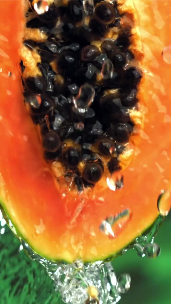 Vannsprut på fersk papaya-halvdel med svarte frø