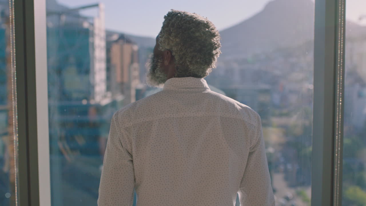 성숙한 아프리카계 미국인 사업가 가 창문 밖 을 바라보며 미래 의 사업 개발 에 대한 아이디어 를 생각 하고 해가 지는 도시 를 바라보며 4k