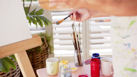 painting on canvas, person holding paintbrush and palette in bright room