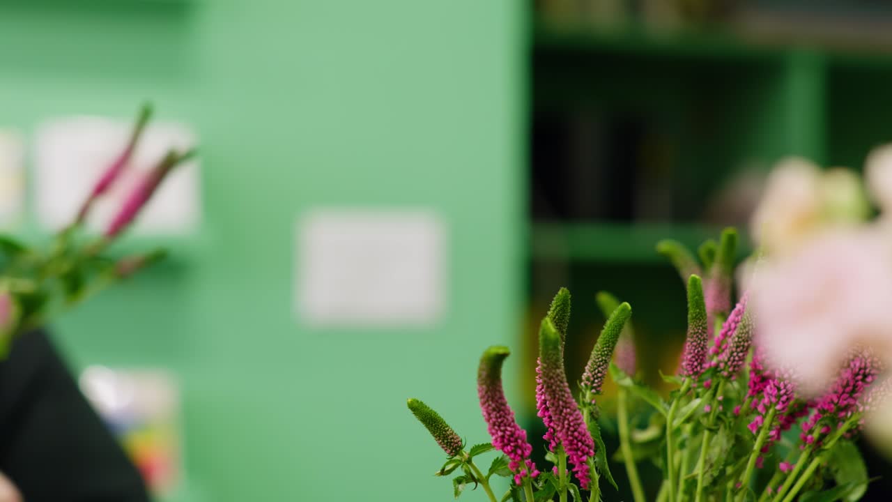 A left-to-right dolly shot showcases vibrant pink Veronica in focus while a florist’s hands are blurred in the background, preparing a stem for an arrangement