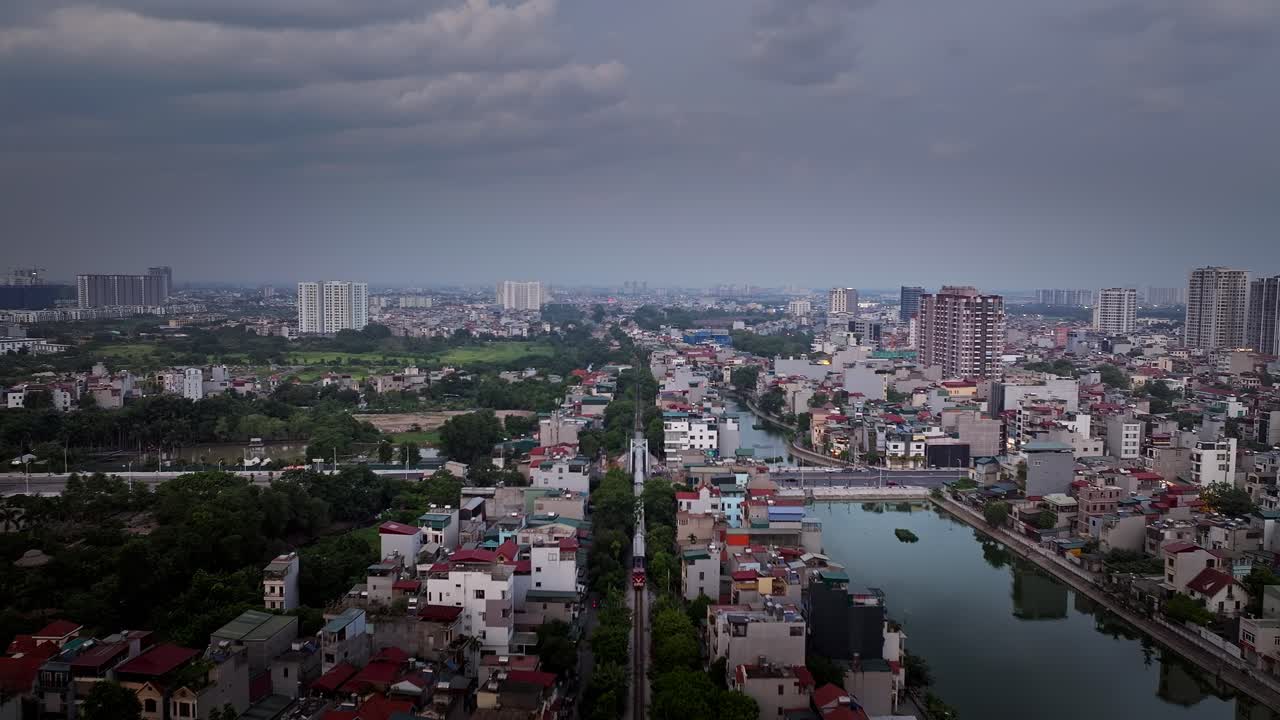 Tracciamento aereo sopra un treno che attraversa il centro di Hanoi, Vietnam, con paesaggio urbano e cielo nuvoloso