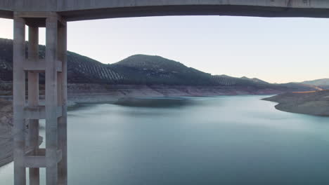 drone flying backwards and under the bridge on the reservoir of iznájar, córdoba, spain