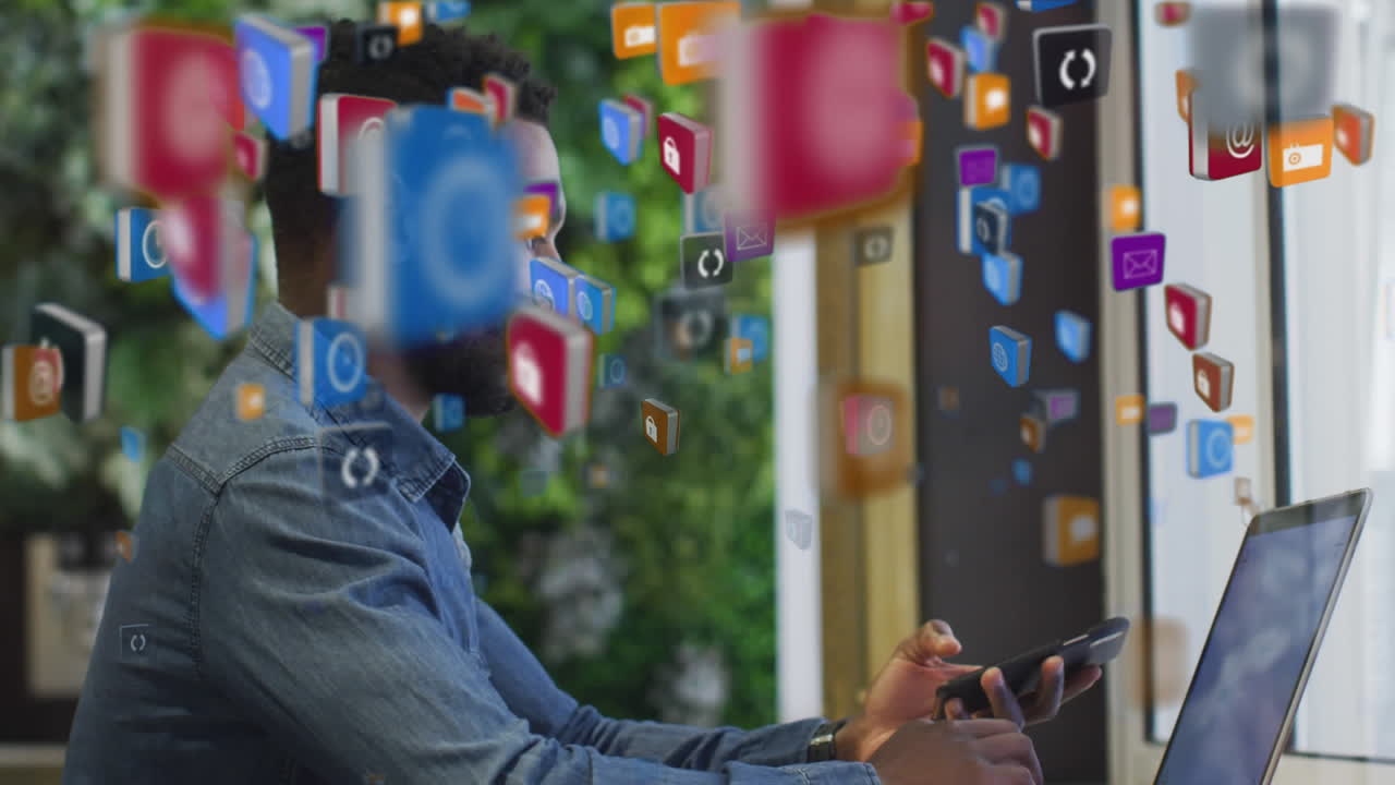 vários ícones digitais flutuando contra um homem afro-americano usando laptop e smartphone