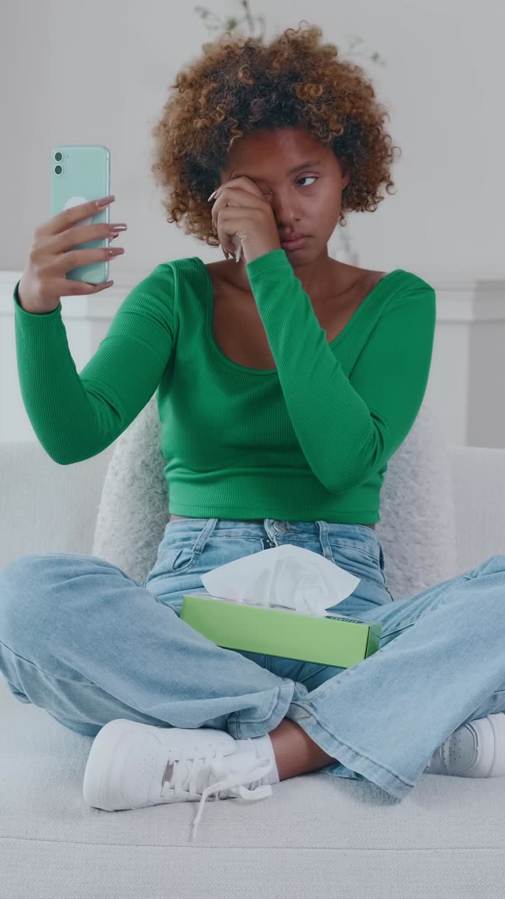 Young woman sitting cross legged on a sofa taking a selfie while looking unwell