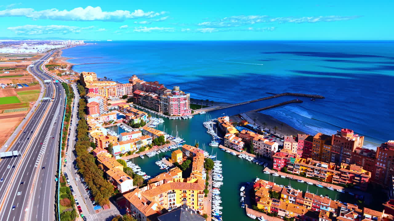 Autostrada a più corsie che corre lungo un colorato complesso portuale residenziale e il blu Mar Mediterraneo. Veduta aerea di un'autostrada costiera che attraversa un resort di lusso sul mare.
