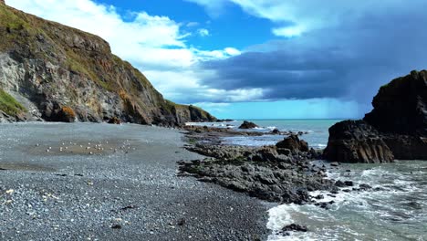 drones épicos volando bajo en una playa con acantilados marinos y formaciones rocosas dramáticas tormenta hacia el mar en la distancia waterford costa de irlanda