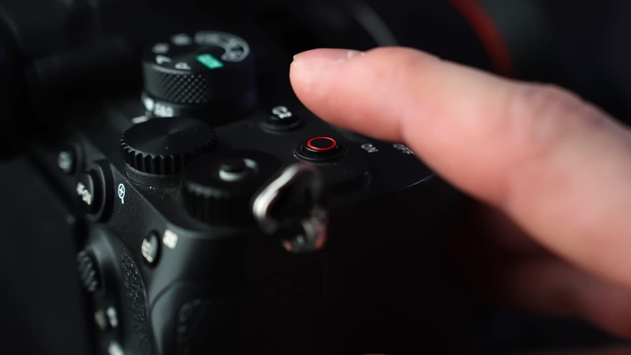 Ein Finger drückt den roten Aufnahme-Knopf auf der Oberseite einer spiegellosen Kamera und startet die Videoaufnahme bei stimmungsvoller Studiobeleuchtung mit weichem Bokeh und geringer Schärfentiefe.