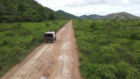 Vista-Aérea-De-Un-Camión-Con-Un-Hombre-Encima-De-La-Cabina-Del-Conductor-Moviéndose-Por-Un-Camino-De-Tierra-En-El-Paisaje-Rural-De-América-Del-Sur