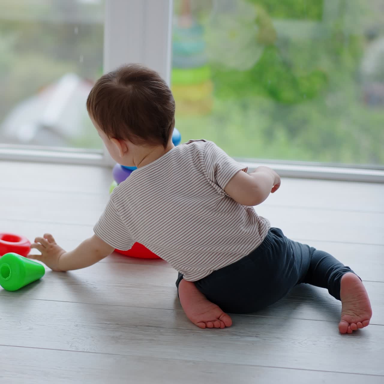 Rear view of Caucasian toddler playing with pyramid. Peaceful child assembling a pyramid on a balcony