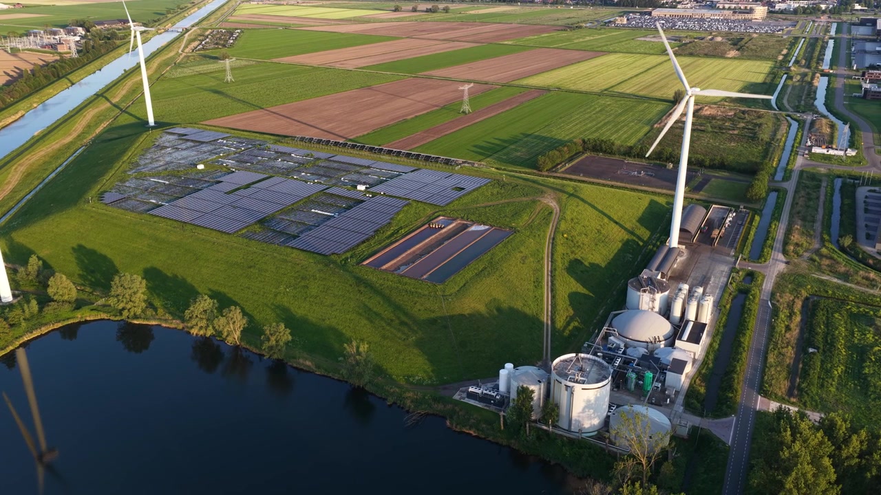 Aerial perspective showcasing a modern renewable energy facility, featuring spinning wind turbines, expansive solar panel fields, and a biogas plant nestled within a lush green rural landscape