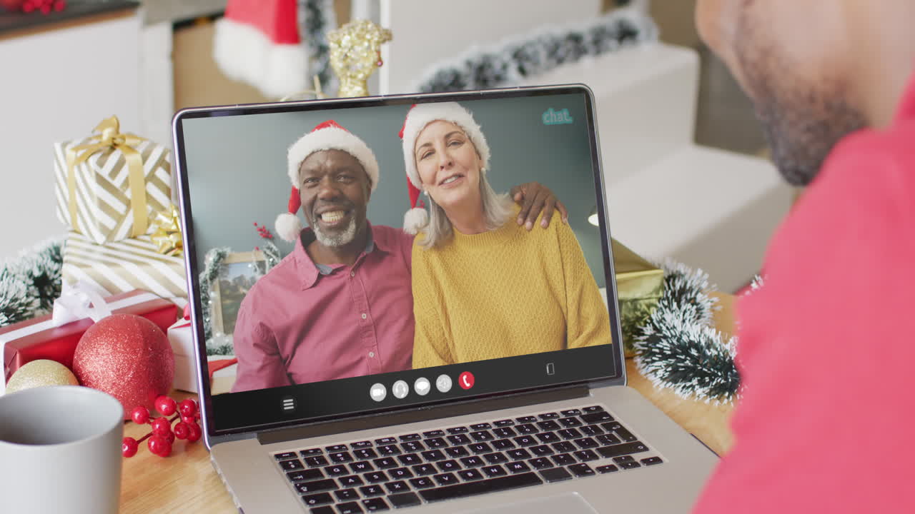 Uomo afroamericano con cappello di Babbo Natale in videochiamata su laptop con una felice coppia multietnica