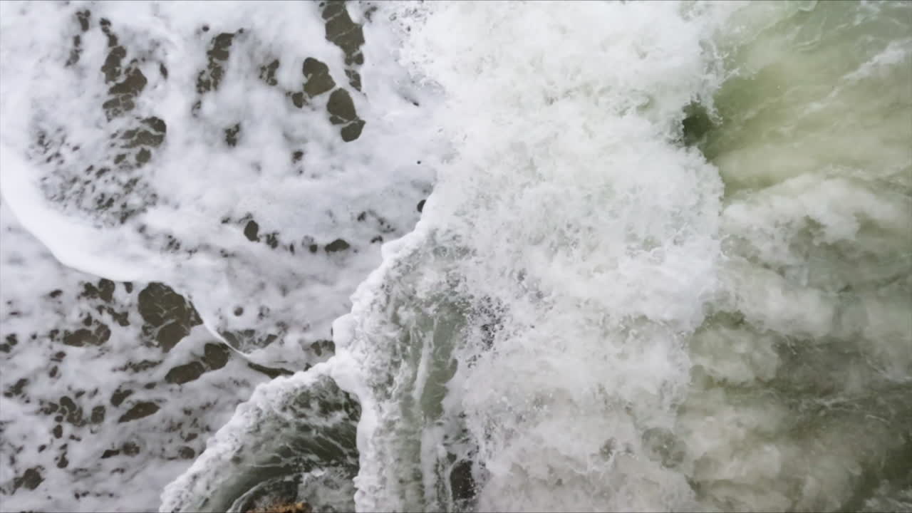 Super slow motion shot of a white foam ocean wave hitting a large dark rock in the sea