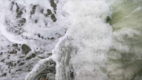 super slow motion shot of a white foam ocean wave hitting a large dark rock in the sea