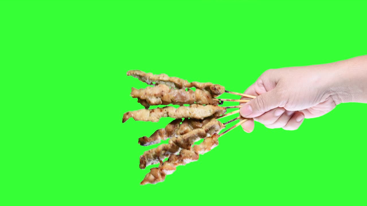 초록색 스크린 배경에 바베큐 사타이 을 들고 있는 손.