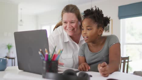 happy caucasian woman and her african american daughter doing homework together