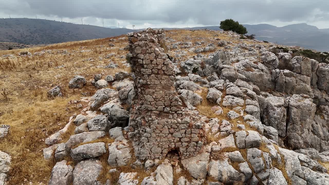 Dron aéreo orbitando una antigua y desgastada torre de piedra en una cresta rocosa cerca de Ronda, España, mostrando ruinas históricas y un paisaje montañoso
