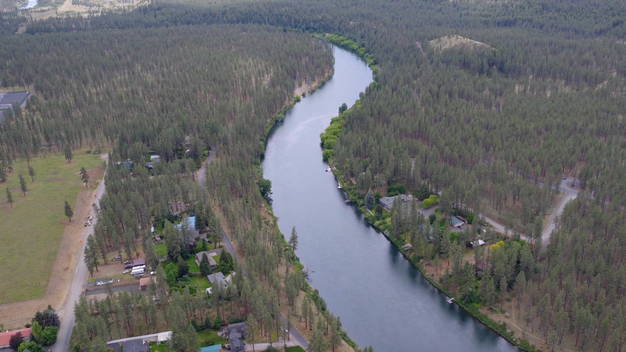 Droneoptagelse af en flod, der bugter sig forbi skovklædte bredder og spredte huse ved søen i udkanten af Spokane, WA