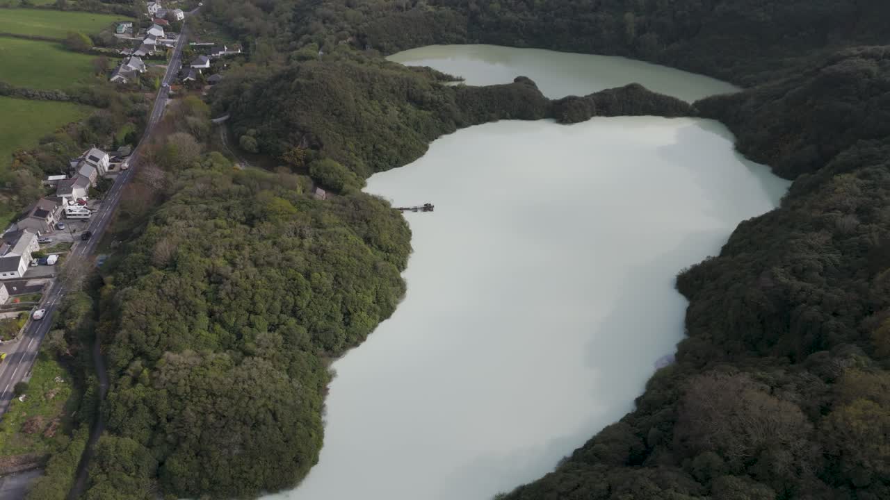 Aerial view of abandoned quarry transformed into milky aqua lake ringed by dense forest, illustrating natural reclamation, mineral sediment coloration and serene wilderness contrast to industry