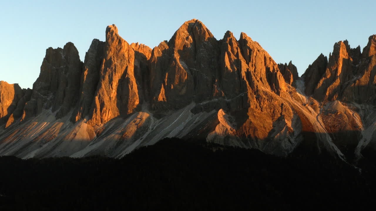 Cinematic aerial view of Dolomites Italy at sunrise, rugged rocky peaks above lush alpine hills and scattered chalets, serene mountain travel landscape nature scenery