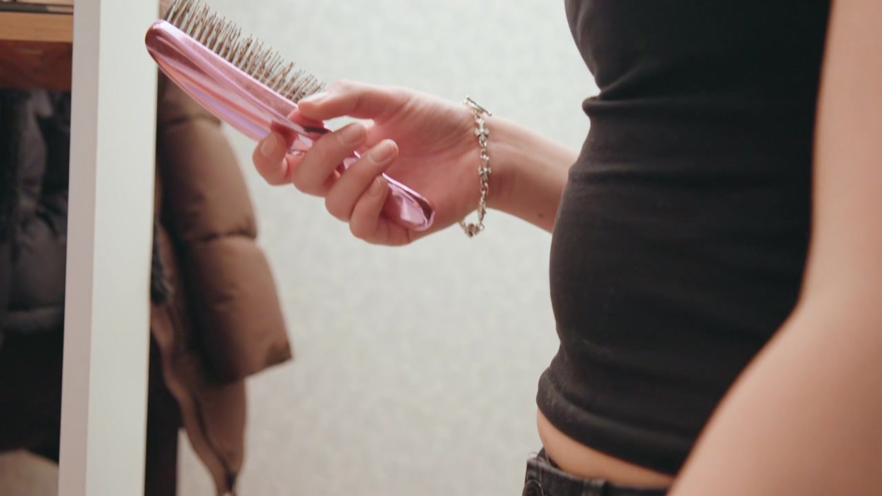 Woman carefully picks hairbrush to style hair. She selects hairbrush to craft her desired hairstyle precisely. Woman intentionally picks her hairbrush from dresser to style her hair meticulously