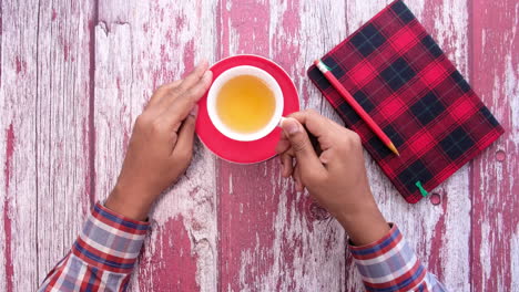 person holding a cup of tea on a red wooden table