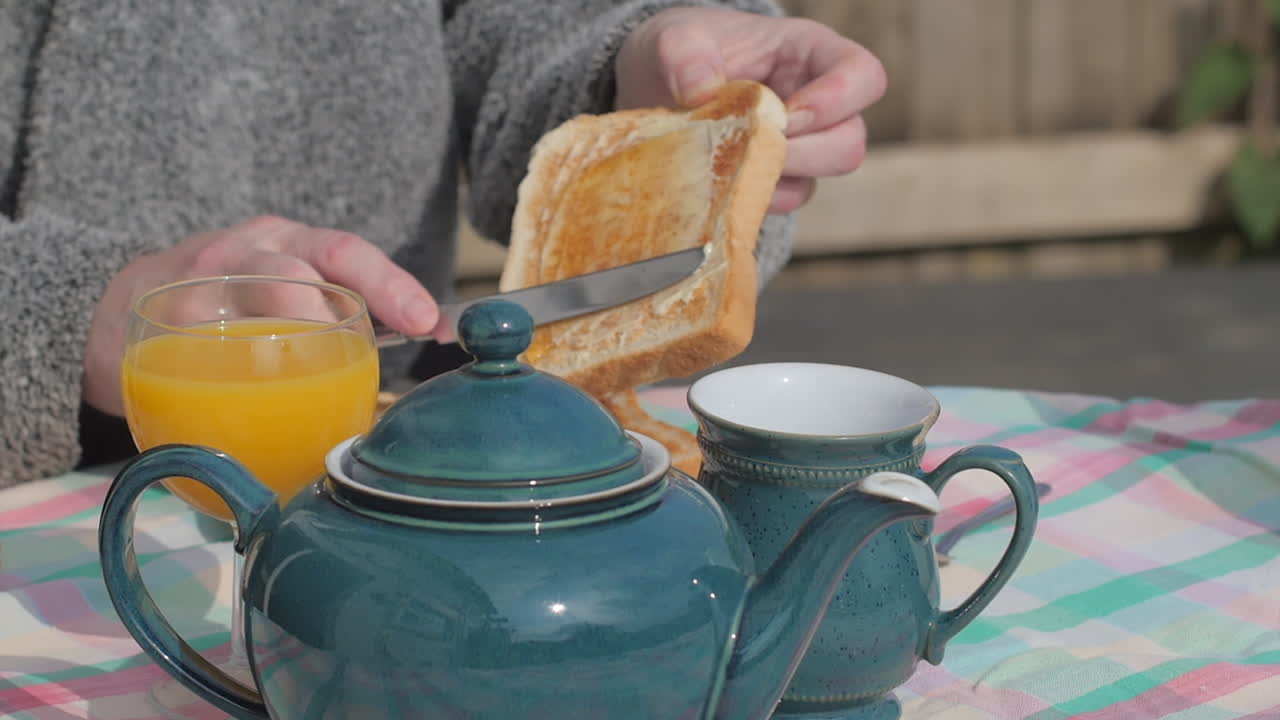 Person smører syltetøy og smør på en skive ristet brød under en engelsk frokost utendørs