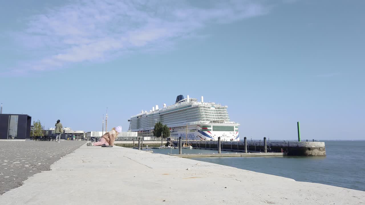 어린 소녀 앉아 땅, 백그라운드에서 거대한 유람선, 리스본, 포르투갈