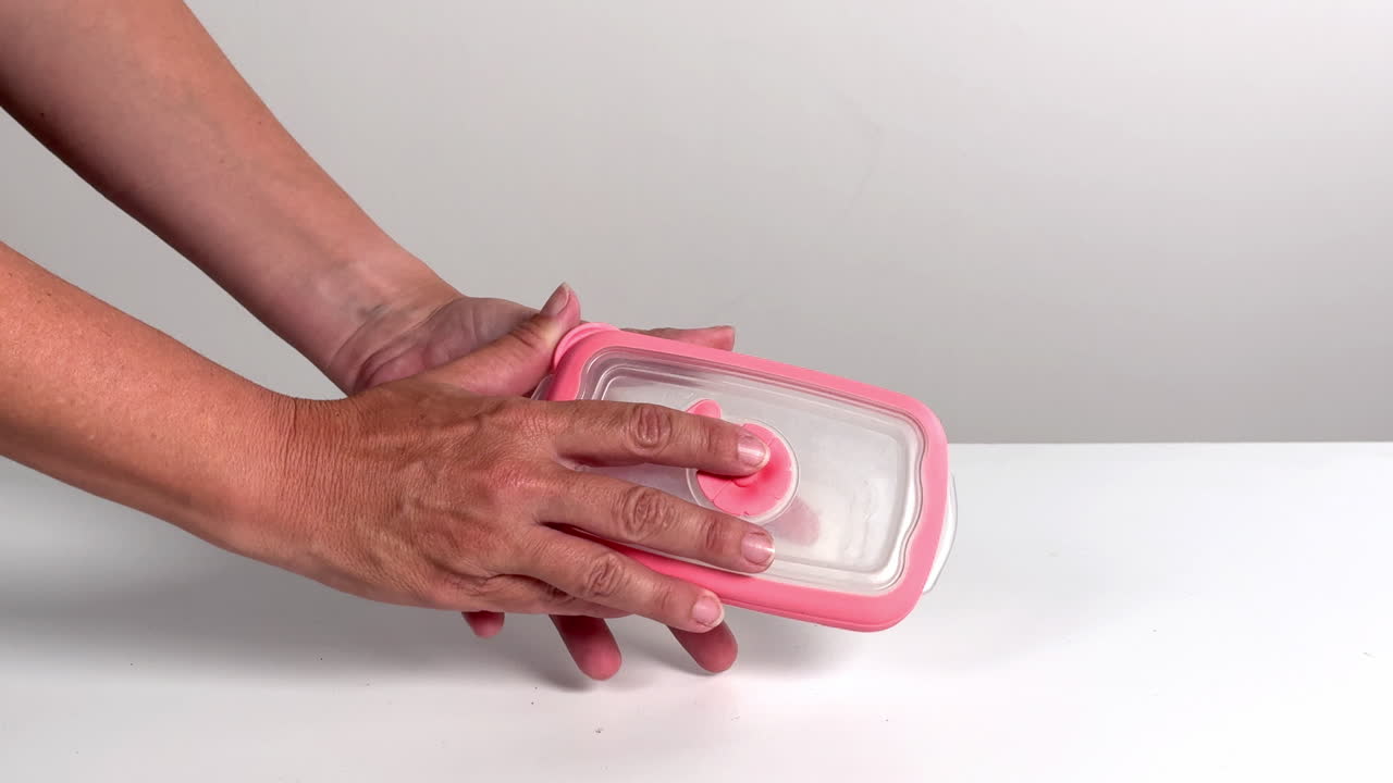 Mani che aprono e chiudono un piccolo contenitore di plastica con coperchio rosa