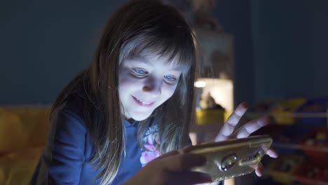 little girl playing with phone in night room is happy and having fun.