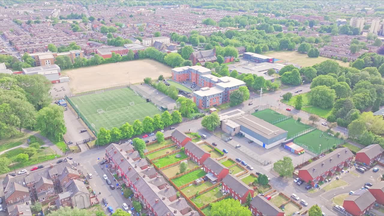 Aerial footage of Dilworth Street, Manchester, showing red-brick terraced homes, university sports fields, tree-lined roads, and the urban sprawl in the University and Ardwick district surroundings