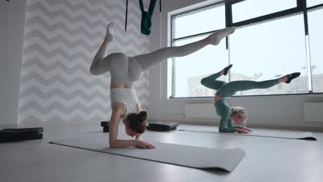 group of young women stretching in gym with windows. two attractive sport girls work out nauka asana boat yoga pose on black mat in fitness class. two women stretching legs together in yoga studio