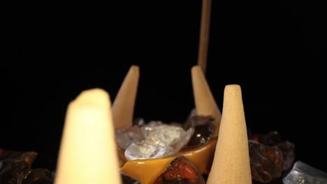 quickly pushing past several unlit incense cones in a decorative rock garden, towards a incense stick that is not smoking