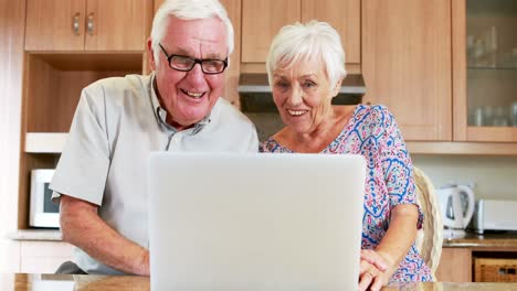 smiling couple using laptop in kitchen