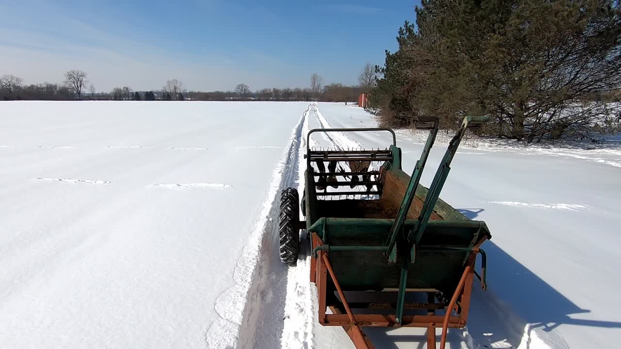En gødningsspreder kører over en snedækket mark på en solrig vinterdag i det sydøstlige Michigan.