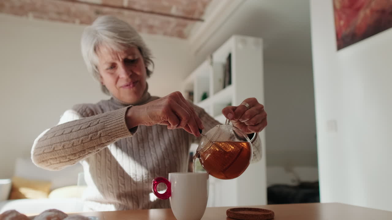 Donna anziana che versa tè caldo da una teiera in una tazza