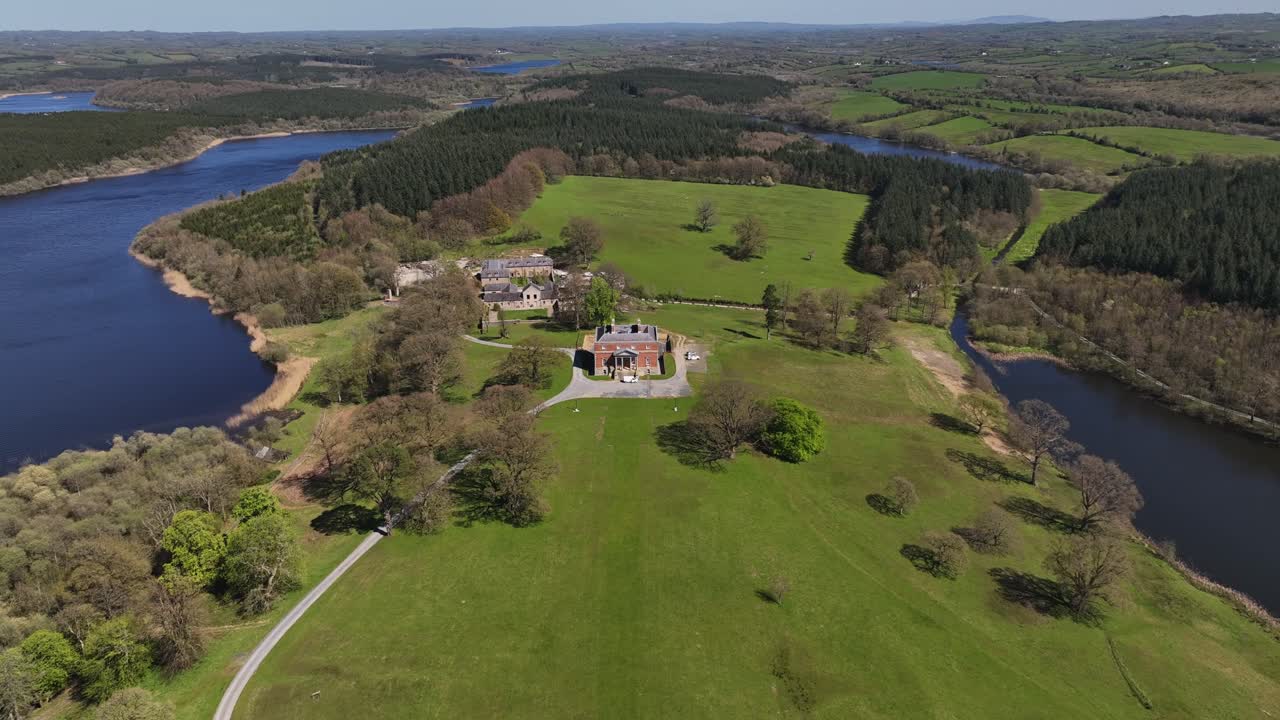 Bellamont House, County Cavan, Ireland, April 2023. Drone orbiting counterclockwise, aerial view of historical building surrounded by scenic lakes, rolling hills and forest.