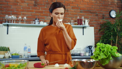 una mujer degustando un bulbo de cebolla cortada, una ama de casa sonriente cocinando verduras.