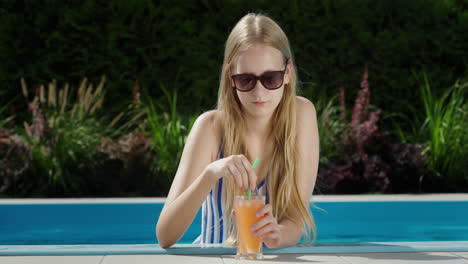 portrait of a teenage girl in the pool with a glass of soft drink