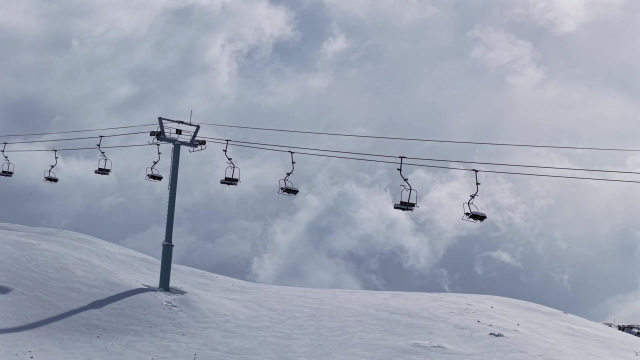 Una seggiovia vuota attraversa piste innevate sotto nuvole drammatiche a Las Leñas Mendoza, con drone che traccia a sinistra.