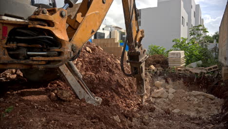movimiento lento de una retroexcavadora con un martillo hidráulico haciendo un agujero para una piscina en un sitio de construcción