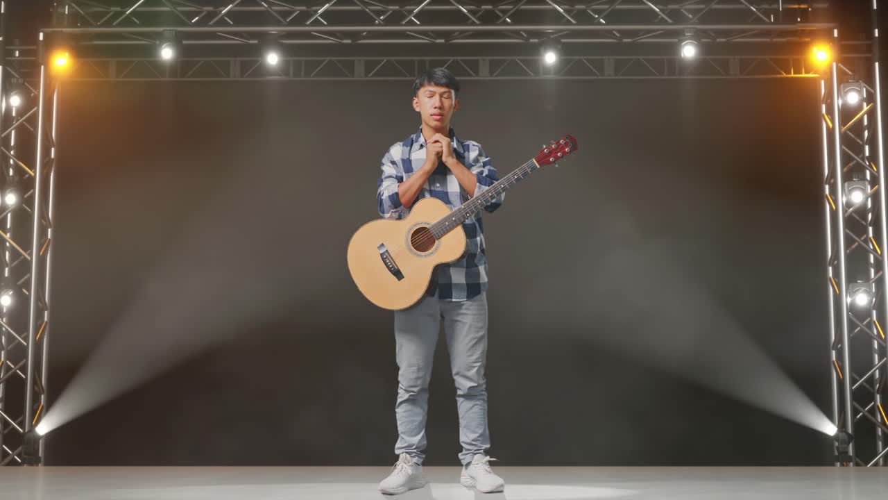 cuerpo lleno de adolescente asiático con guitarra rezar por algo en el escenario